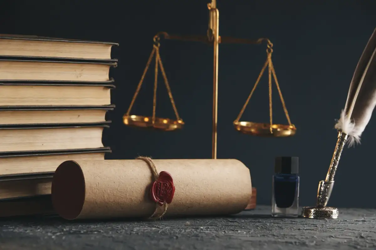 Waga sprawiedliwości, księgi i pieczęć na zwoju. Kto opłaca notariusza przy sprzedaży mieszkania? Zazwyczaj kupujący.