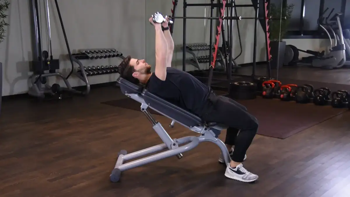 Mężczyzna wykonuje ćwiczenie incline dumbbell press na ławce skośnej, podnosząc ciężarki nad klatkę piersiową.