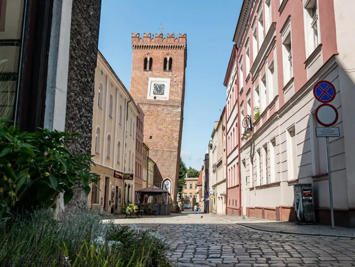 Wieża zegarowa w Ząbkowicach Śląskich na tle kamienic i brukowanej ulicy.