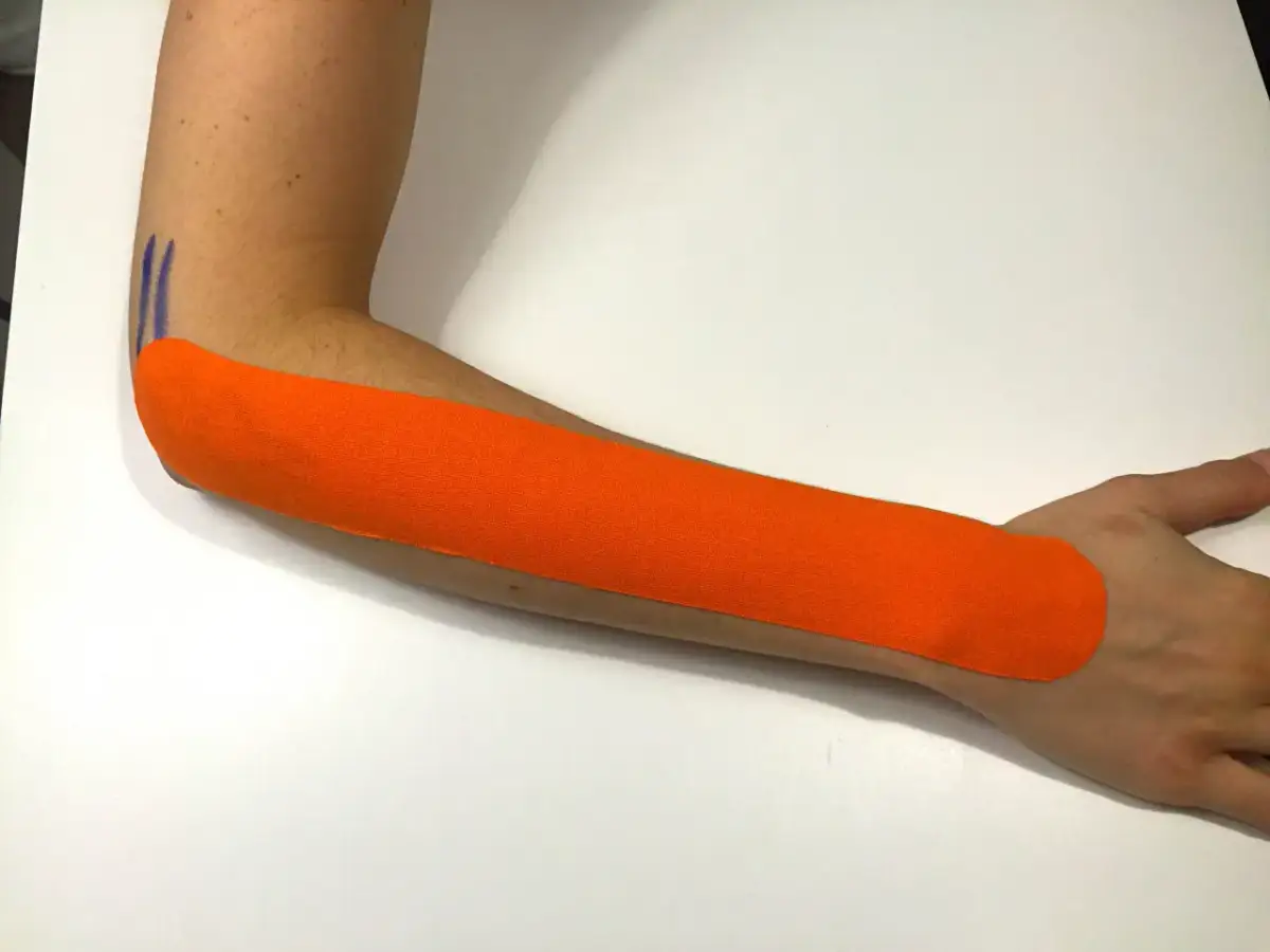 Pomarańczowy plaster kinezjotaping na przedramieniu, wspierający ćwiczenia na łokieć tenisisty.