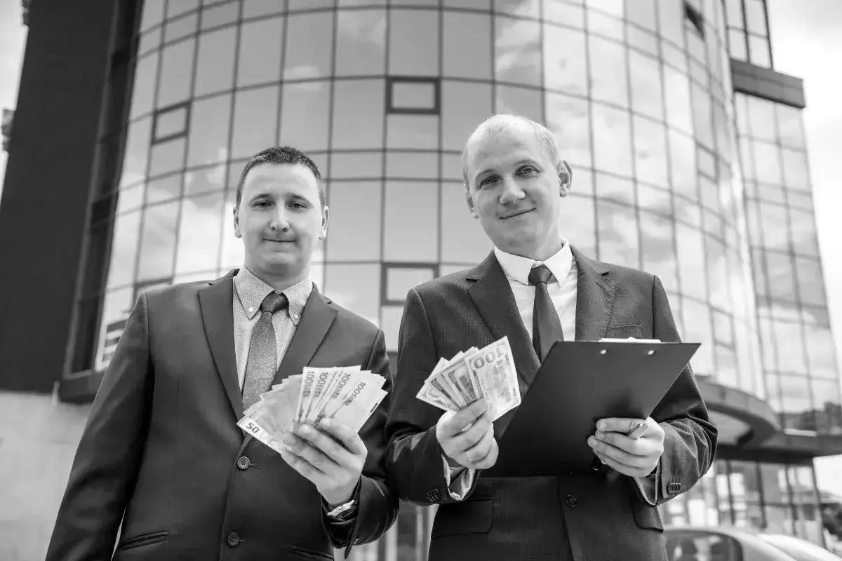 Dwóch mężczyzn w garniturach trzyma pieniądze i dokumenty. Ich aktywa rosną.