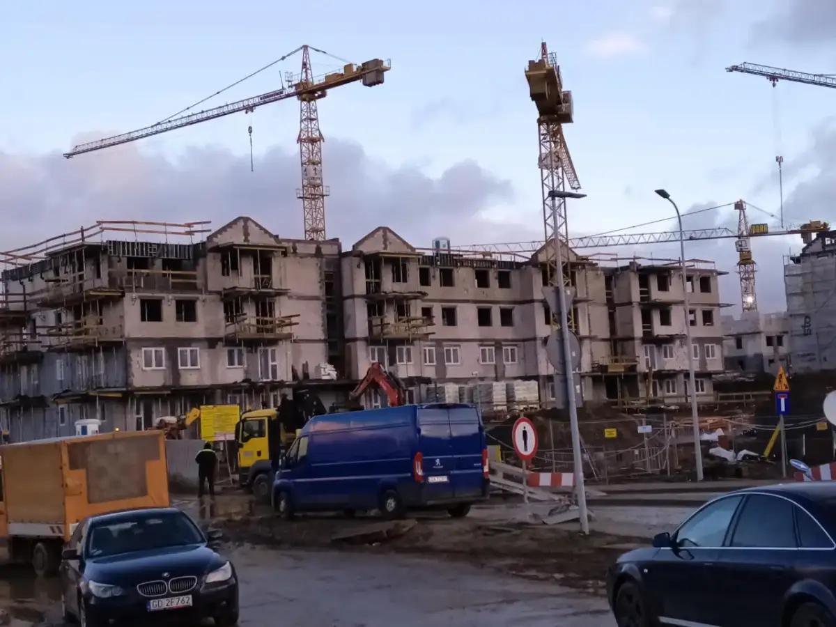 Budowa bloków mieszkalnych w Gdańsku. W tle dźwigi budowlane, na pierwszym planie samochody i maszyny budowlane. Ceny mieszkań gdańsk mogą być wysokie.