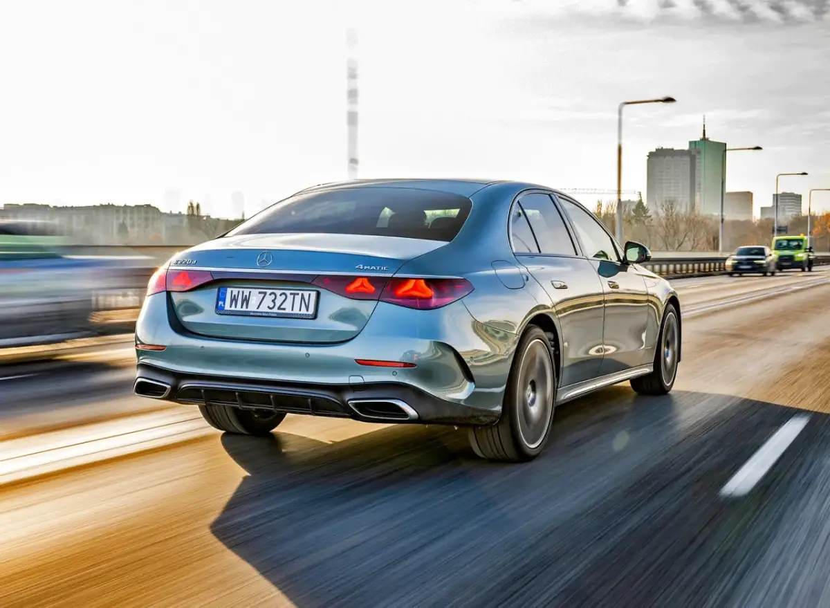 Elegancki, błękitny Mercedes E220d 4MATIC pędzi autostradą, mijając miejską panoramę.