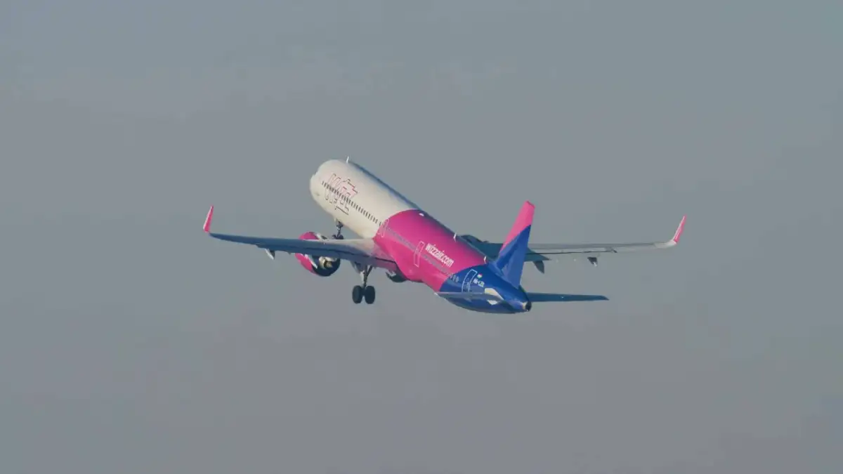 Samolot Wizz Air w różowo-niebieskich barwach startuje na tle szarego nieba.