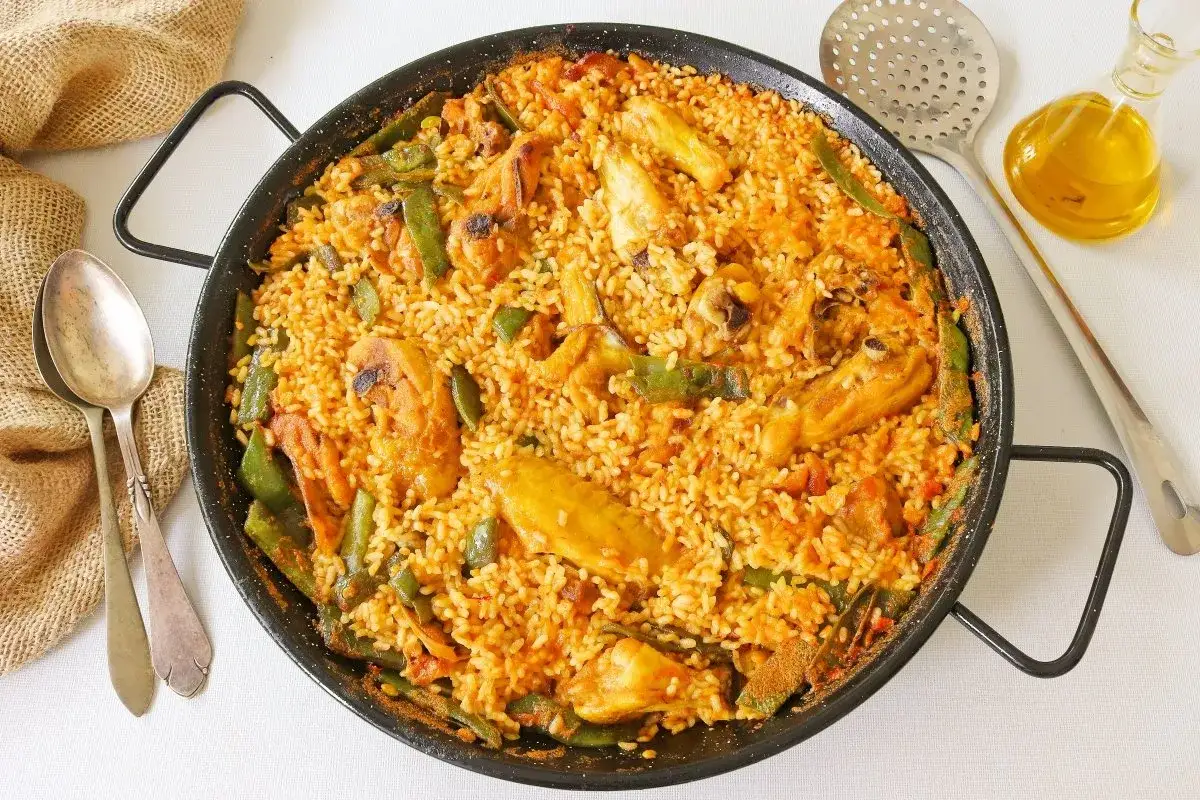 Paella de pollo recién hecha, con trozos de pollo dorado, judías verdes y arroz sabroso en una paellera.