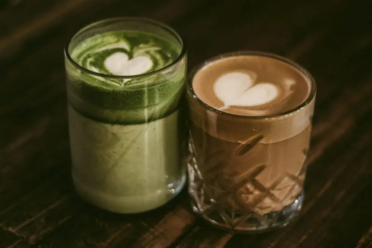 Dwa napoje w szklankach: zielona matcha i kawa z pianką w kształcie serca.