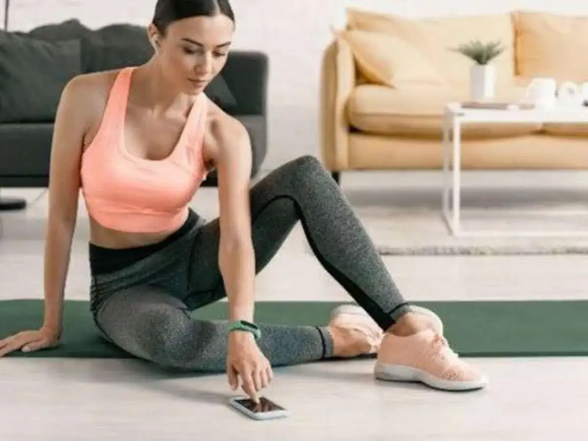 Frau in Sportkleidung sitzt auf einer Matte und bedient ihr Smartphone.