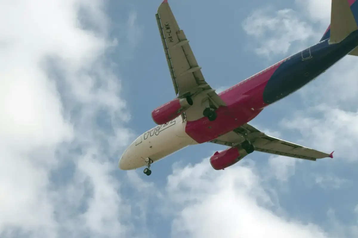Samolot Wizz Air z wysuniętym podwoziem na tle nieba z chmurami.