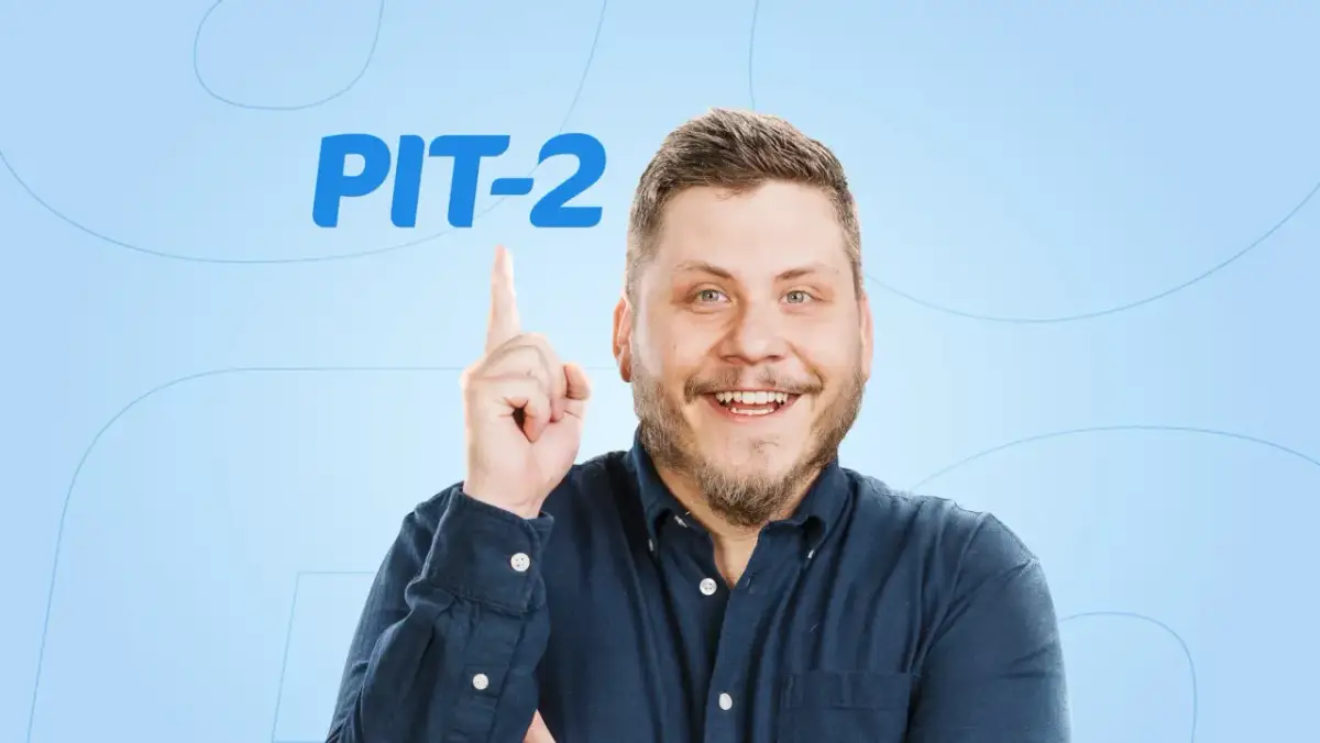Uśmiechnięty mężczyzna w granatowej koszuli wskazuje palcem na napis PIT-2.