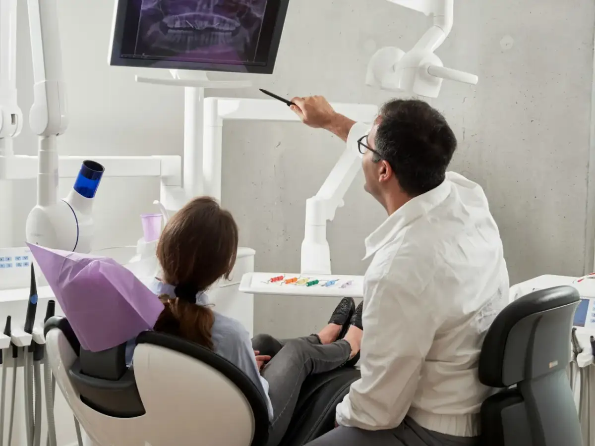 Dentysta omawia z pacjentką zdjęcie RTG, wyjaśniając przebieg leczenia. Ciekawe, ile zarabia dentysta za taką troskę o zdrowie pacjentów.