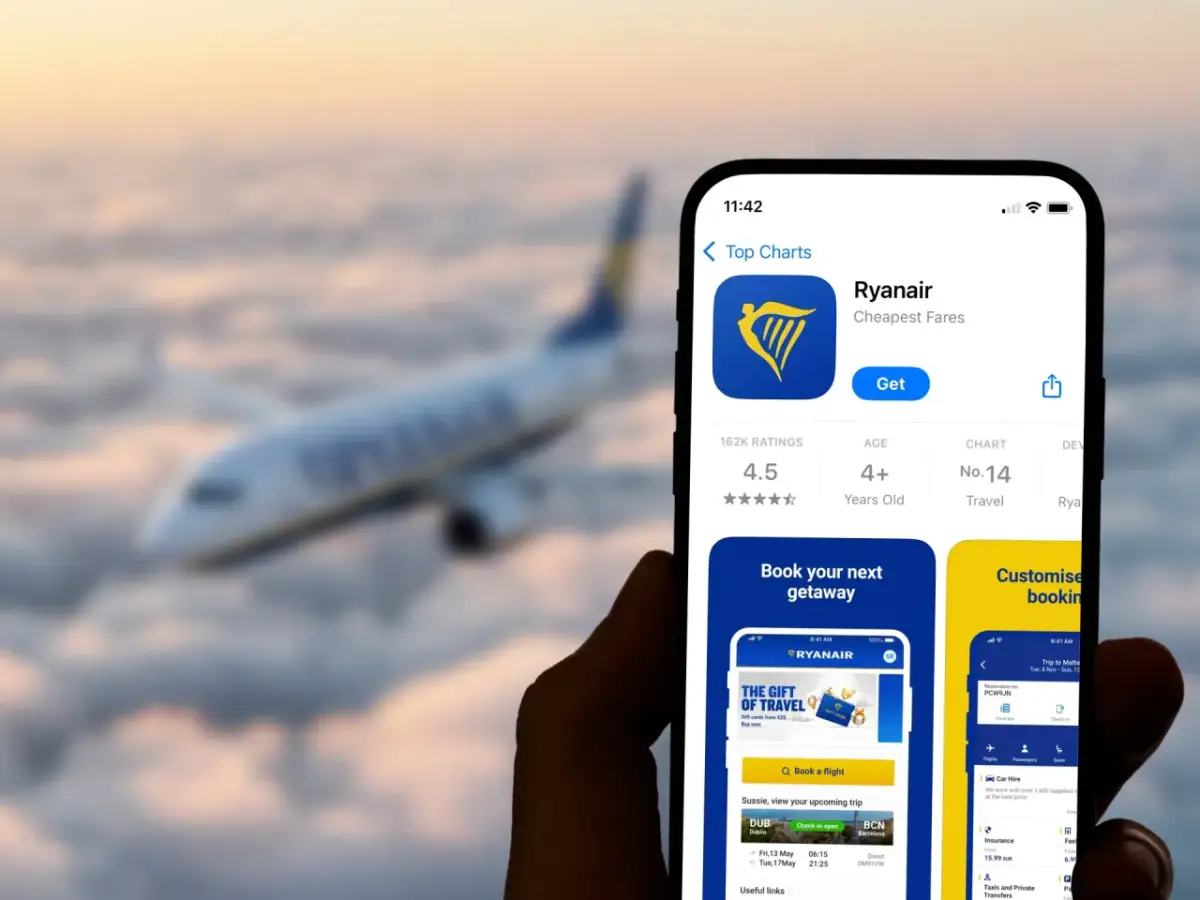 Dłoń trzyma smartfon z aplikacją Ryanair na tle samolotu lecącego nad chmurami.