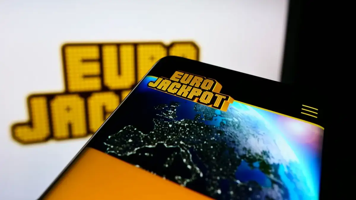 Logo Eurojackpot na ekranie telefonu z widokiem Europy nocą.
