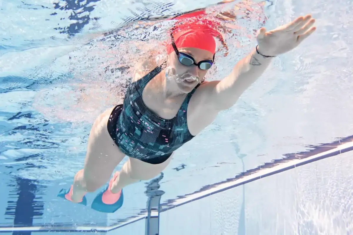 Kobieta w czerwnym czepku i okularach pływackich ćwiczy, jak pływać kraulem i się nie męczyć, używając płetw.