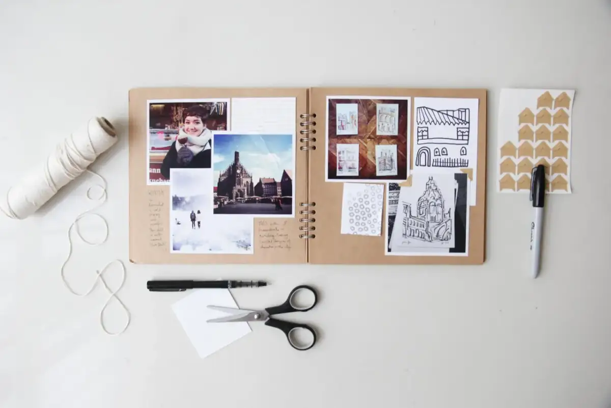 Oto przykład, co to jest scrapbooking: otwarta księga z przyklejonymi zdjęciami, rysunkami i notatkami, obok nożyczki, pisak i sznurek.