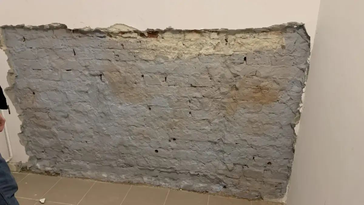 Fragment odsłoniętej, starej ceglanej ściany z szarym tynkiem i fragmentami żółtego podkładu.