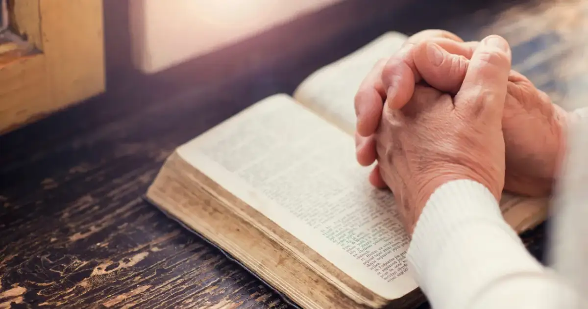 Dłonie złożone nad otwartą księgą, której strony zawierają tekst apostolski.