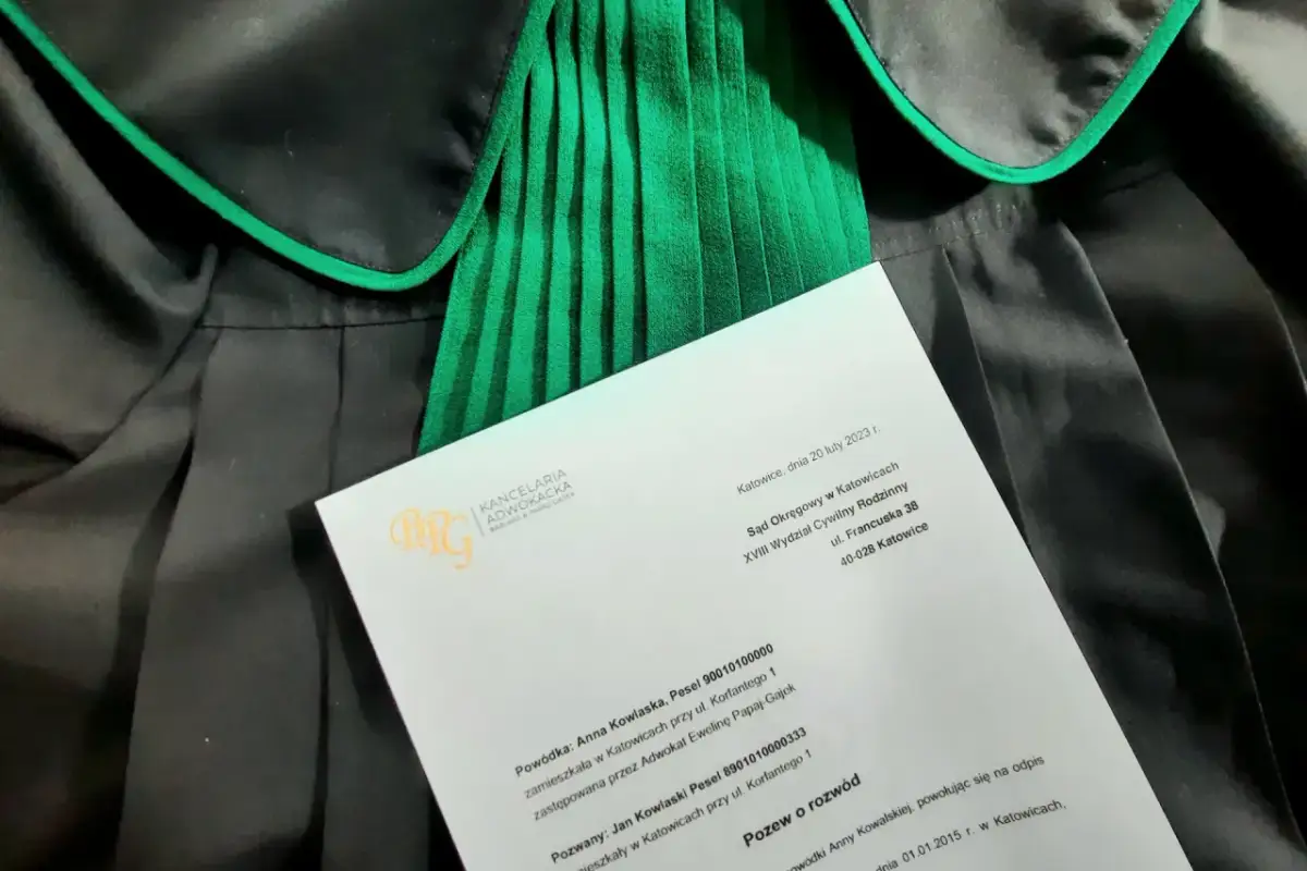 Dokument z Kancelarii Adwokackiej, zawierający wniosek o rozwód cywilny, leży na togach prawniczych.