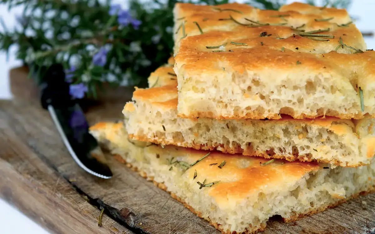 Rebanadas de masa de pizza casera con romero, apiladas sobre una tabla de madera rústica.