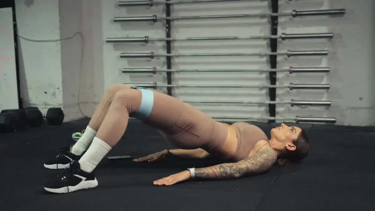 Kobieta wykonuje ćwiczenie glute bridge z taśmą oporową na udach.