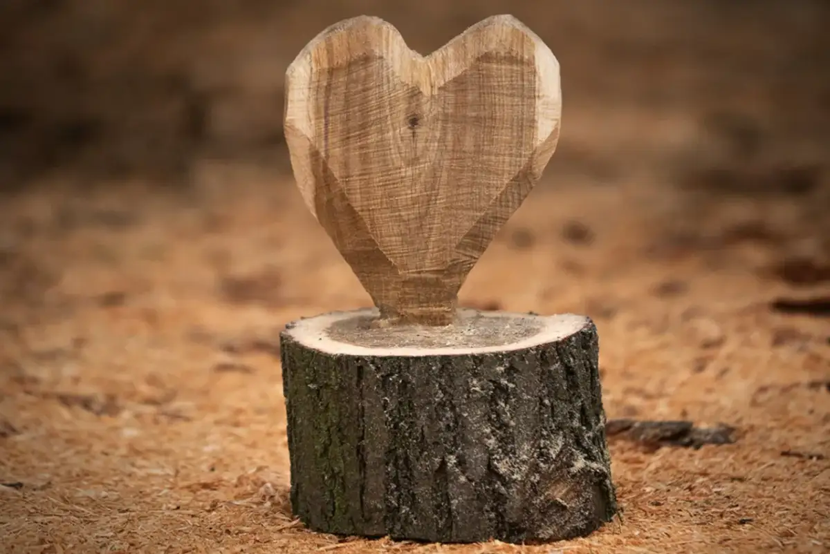 Holzskulptur in Herzform auf einem Baumstumpf, umgeben von Holzspänen.
