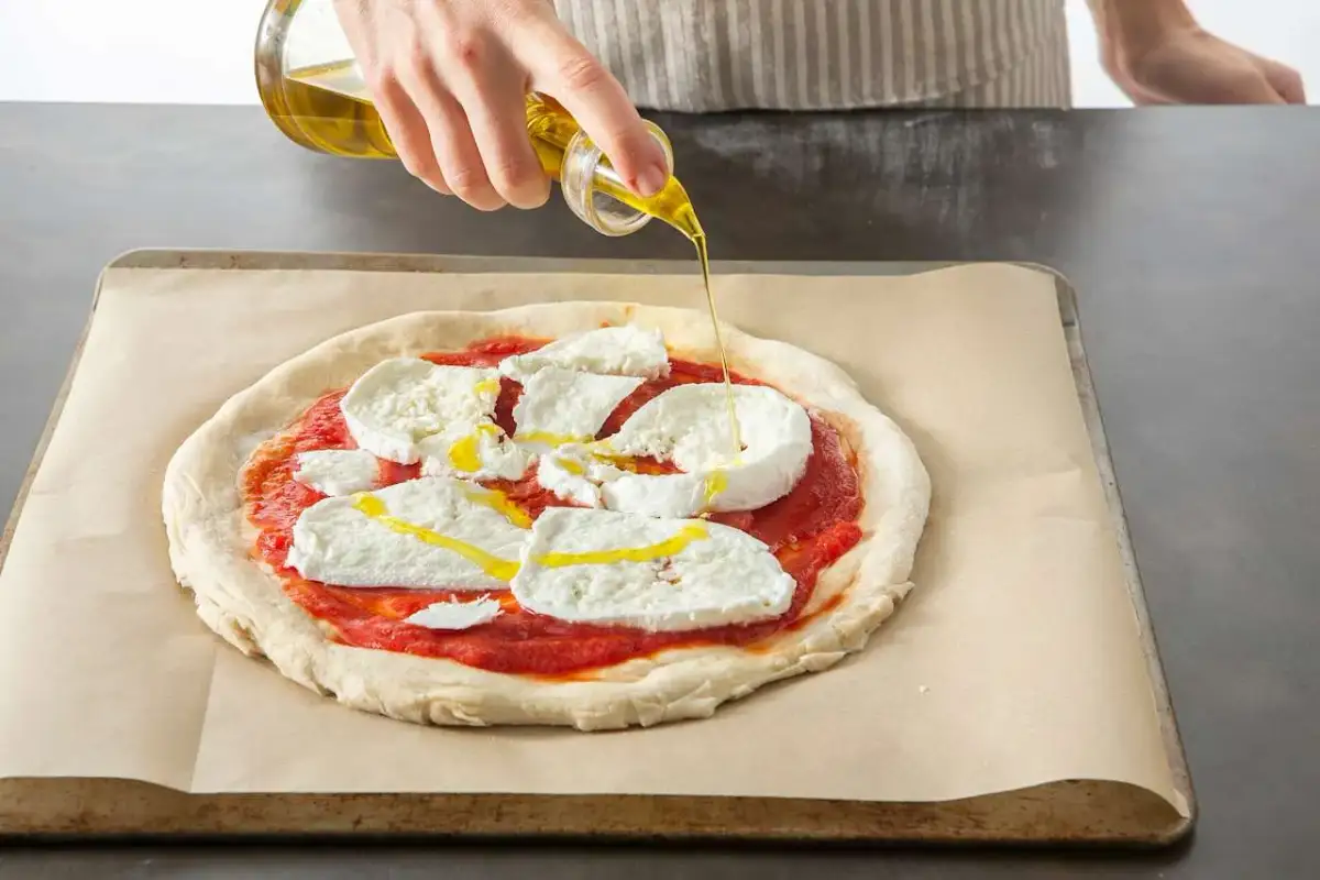Oliwa z oliwek spływa na pizzę z mozzarellą i sosem pomidorowym, przygotowywaną w Thermomixie.