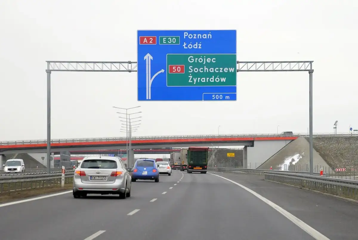 Autostradą A2 w kierunku Poznania i Łodzi. Znak informuje o minimalnej prędkości na autostradzie i zjeździe na Grójec, Sochaczew, Żyrardów za 500 m.
