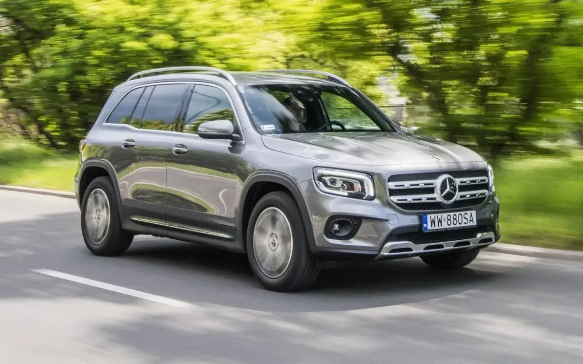 Szary Mercedes GLB 200 jedzie po drodze, otoczony zielenią drzew.