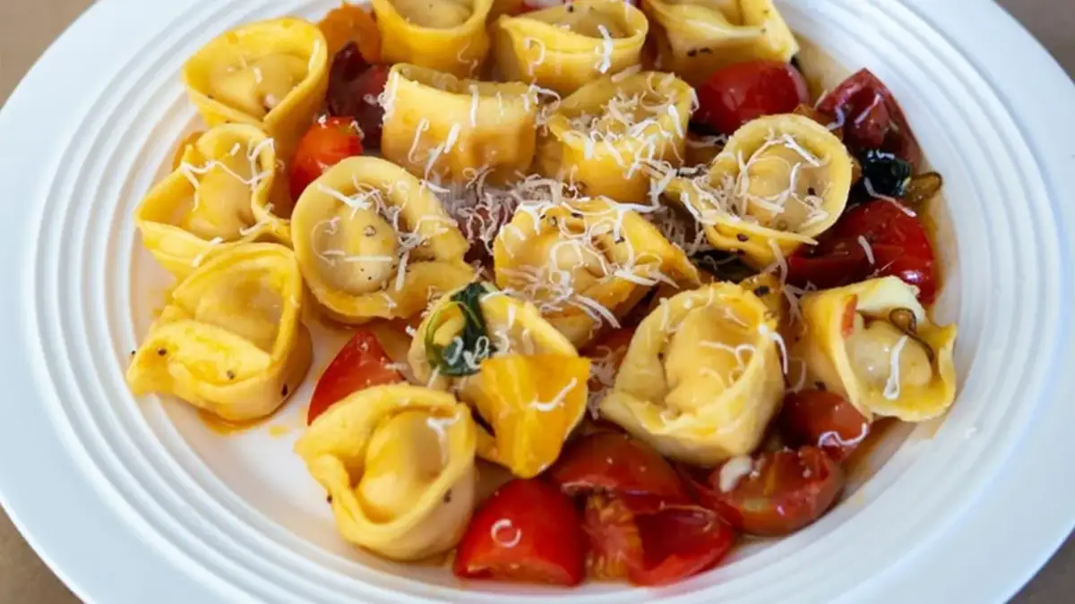 Talerz pełen tortellini z pomidorkami koktajlowymi i startym parmezanem.