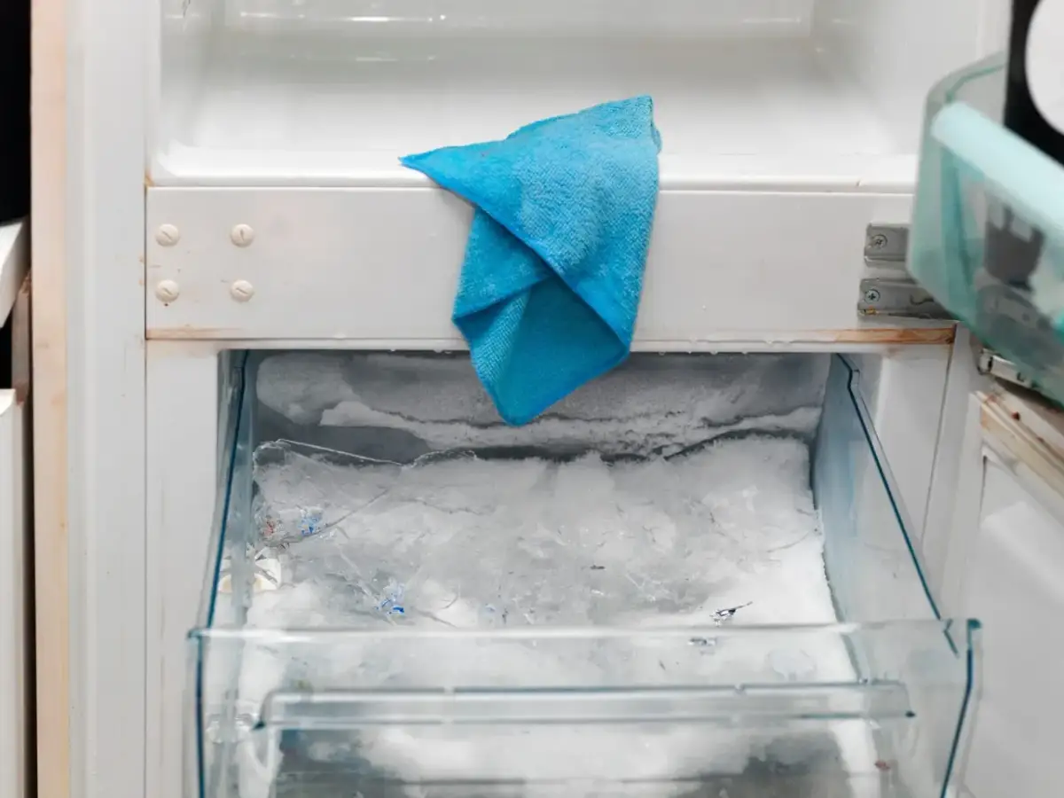 W zamrażarce lodówki no frost nagromadził się lód, a niebieska ściereczka czeka na rozmrożenie.