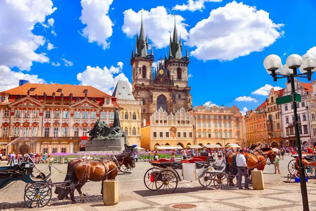 Rynek w Pradze z kościołami, kamienicami i dorożkami konnymi.