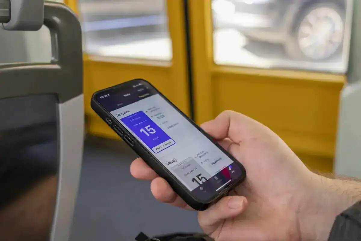 Dłoń trzyma smartfon z aplikacją transportową pokazującą bilet 15-minutowy.