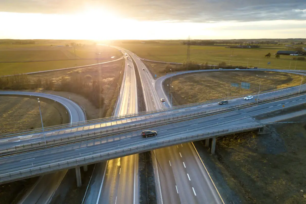 Widok z lotu ptaka na węzeł autostradowy o zachodzie słońca, z samochodami na jezdni.