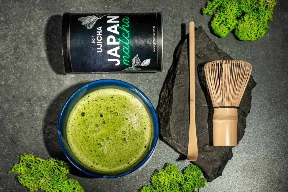 Zestaw do parzenia matcha: puszka z zieloną herbatą, spieniony napój w miseczce, bambusowa miotełka (chasen) i łopatka (chashaku).