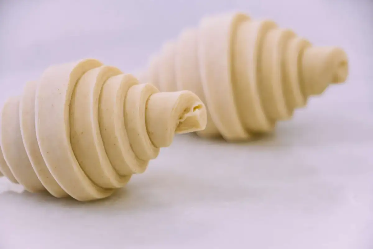 Dos croissants de mantequilla crudos, con sus capas visibles, listos para hornearse y deleitar.