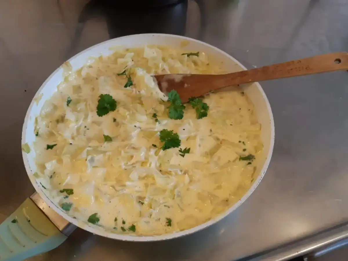 Krämig stuvad vitkål i en panna, garnerad med persilja. En klassisk svensk rätt som doftar hemtrevnad.