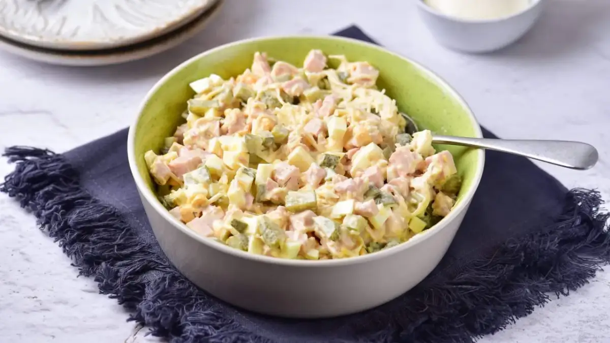 Sałatka z selera konserwowego z szynką, jajkiem i ogórkiem, wymieszana z majonezem, prezentuje się apetycznie w misce.