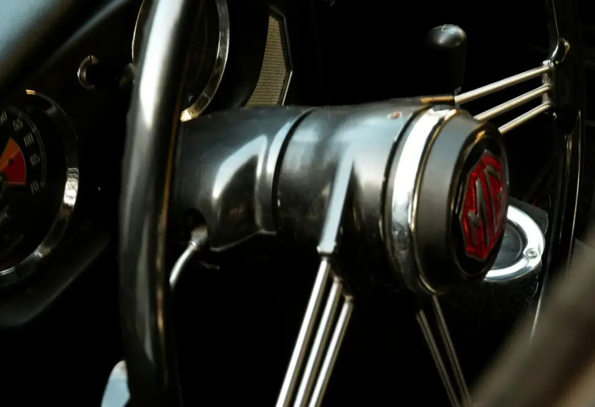 Wnętrze klasycznego MG. Kierownica z chromowanymi szprychami i emblematem MG. Słychać metaliczny pisk przy skręcaniu.