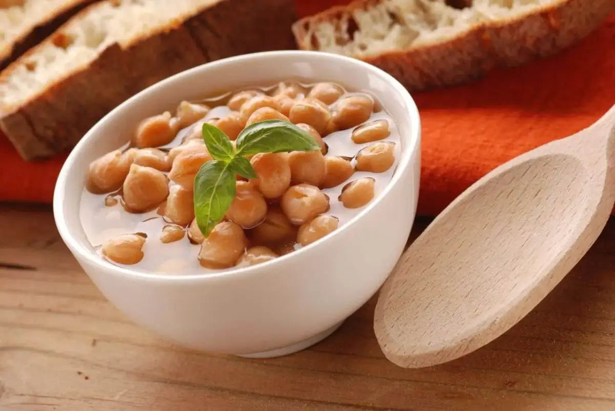 Miseczka ciecierzycy z bazylią, obok kromki chleba i drewniana łyżka.