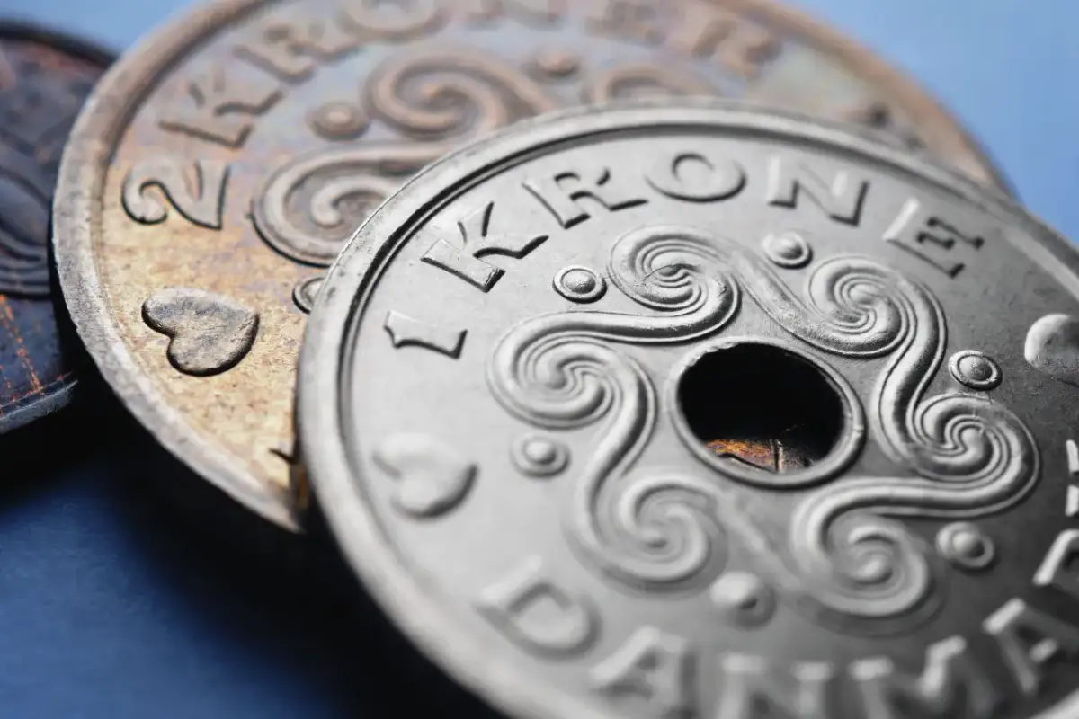 Dwie monety, jedna srebrna z napisem "1 KRONE DANMARK" i otworem pośrodku, druga miedziana z sercem. DKK jaka to waluta?