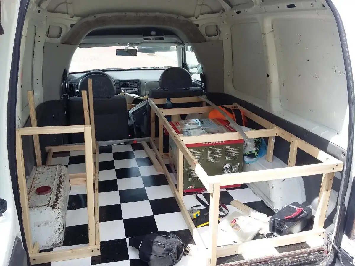 Wnętrze vana przerabiane na minicamper. Drewniana konstrukcja łóżka, szachownica na podłodze, skrzynka narzędziowa.