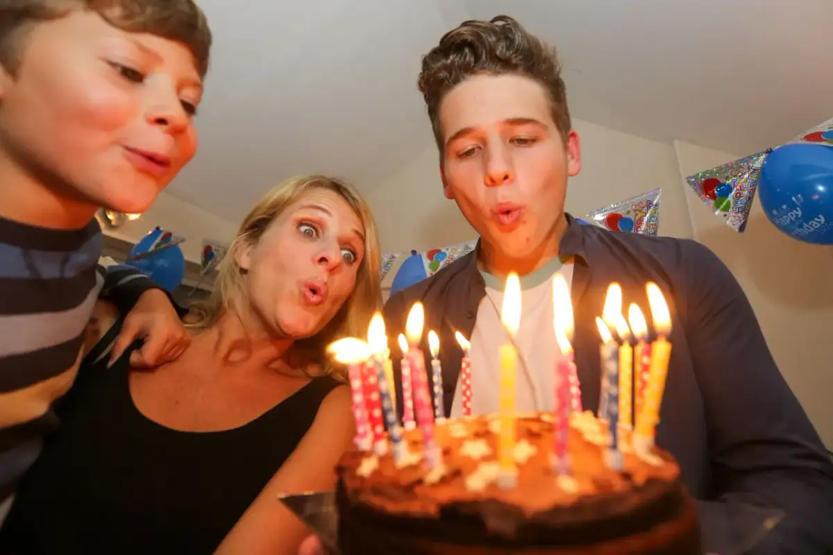 Rodzina zdmuchuje świeczki z tortu urodzinowego.