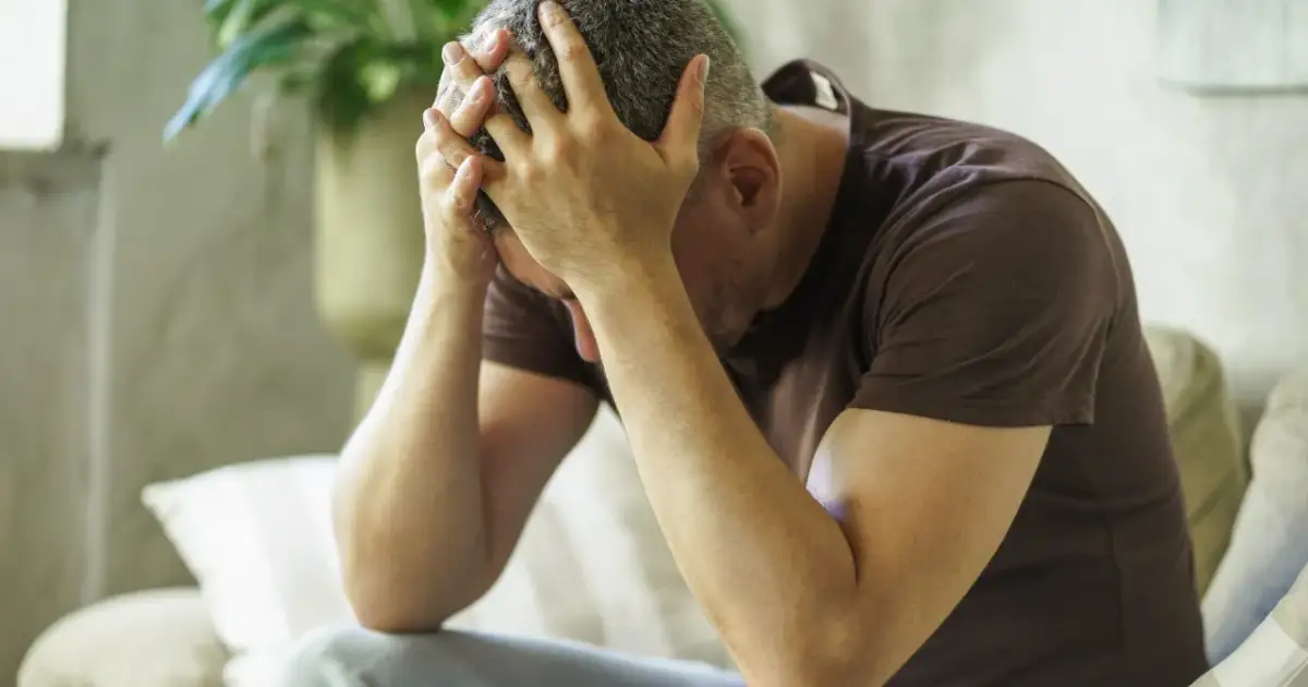 Mężczyzna z rękami na głowie, pogrążony w myślach. Czy to jest febu?