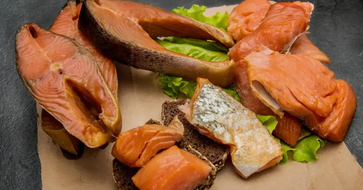 Kawałki wędzonego łososia na liściach sałaty i ciemnym pieczywie. Czy łosoś wędzony jest zdrowy? Tak, to bogactwo kwasów omega-3.