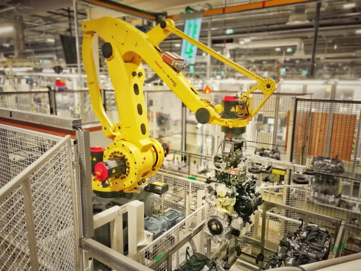 Żółty robot przemysłowy FANUC M-410iC pracuje nad montażem silnika, uosabiając filozofię kaizen toyota w nowoczesnej fabryce.