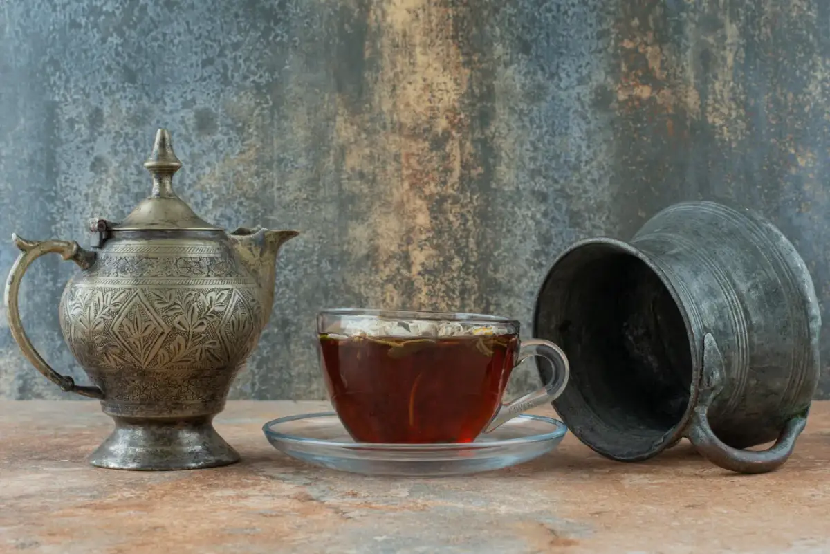 Stary, zdobiony czajniczek i szklanka z herbatą na tle rustykalnej ściany.
