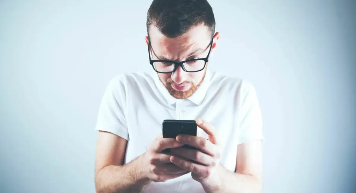 Zastanawiasz się, skąd firma windykacyjna ma Twój numer telefonu? Mężczyzna w okularach patrzy zdezorientowany na ekran smartfona.