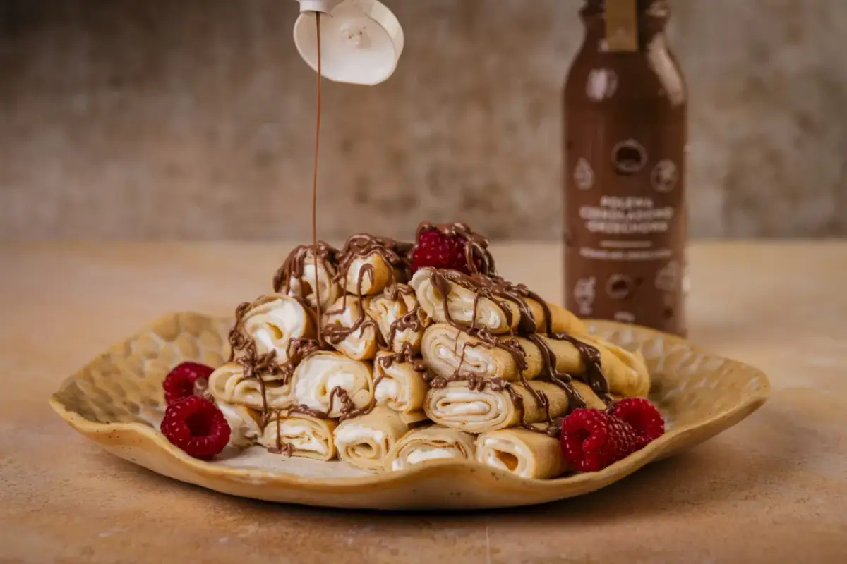 Rolowane naleśniki z serkiem mascarpone, polane czekoladą i ozdobione malinami. Pyszny deser gotowy do zjedzenia!