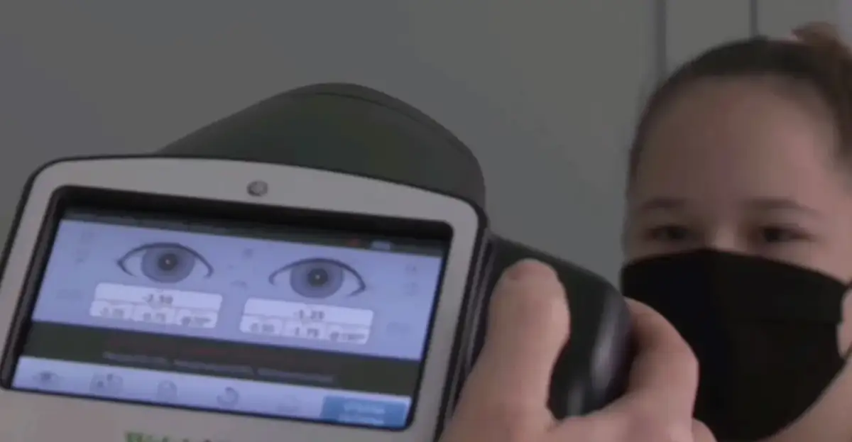 Osoba w masce na twarzy bada wzrok za pomocą urządzenia z ekranem wyświetlającym oczy i parametry.