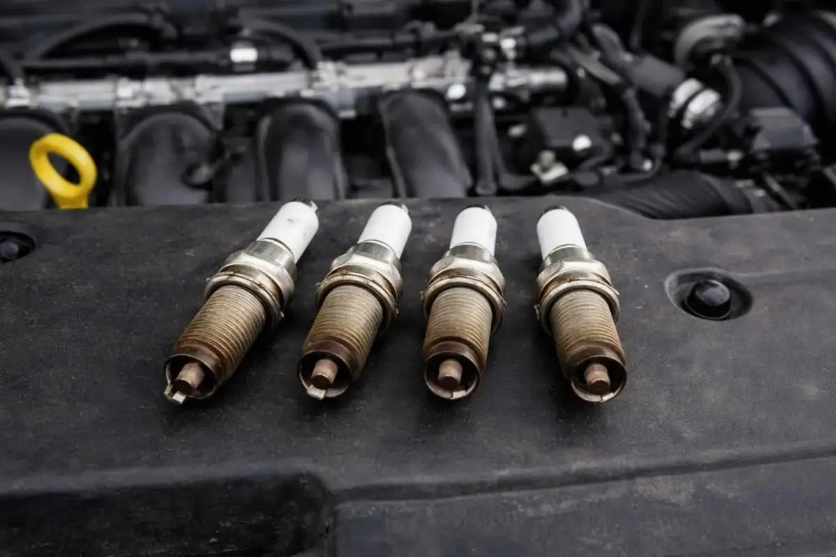 Cztery świece zapłonowe leżą na pokrywie silnika. Zastanawiasz się, co ile wymiana świec w benzynie? Sprawdź zalecenia producenta!