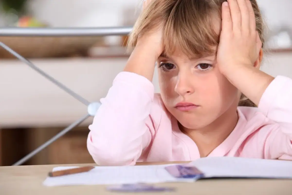 Zmartwiona dziewczynka z rękami na głowie, przy biurku z zeszytem. Czy to oznaka, że ferrytyna norma u dzieci jest nieprawidłowa?